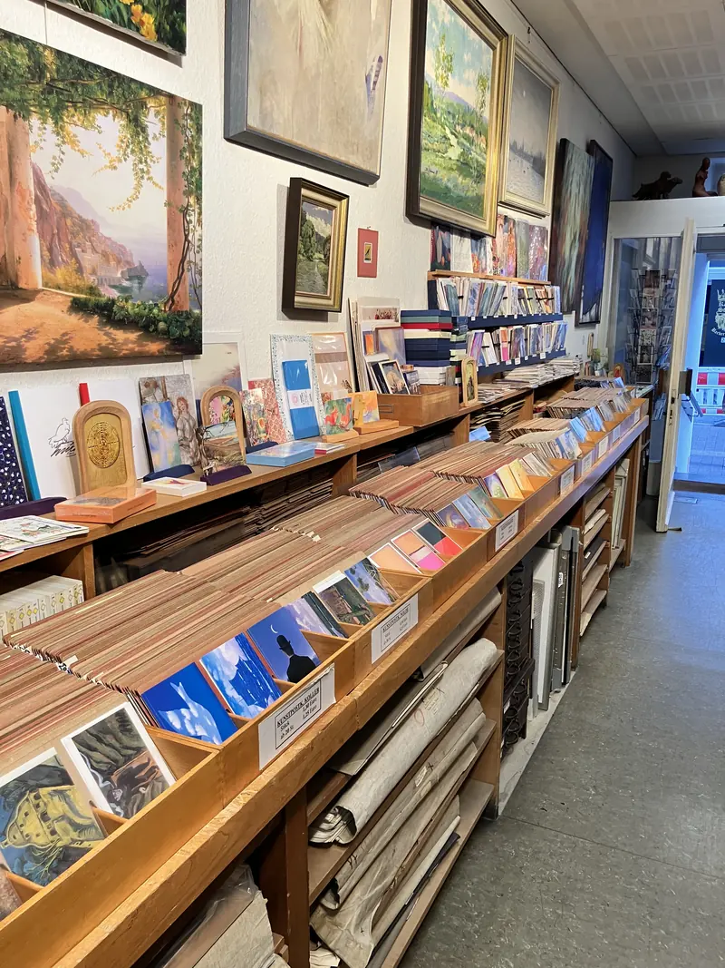 Longs présentoirs en bois remplis de cartes postales d’art, classées par artiste
