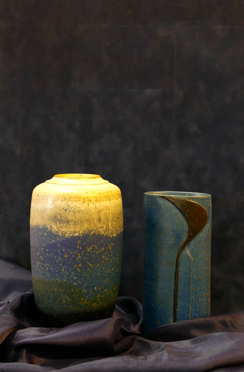 Deux vases en céramique, jaune et bleu, sur un tissu sombre