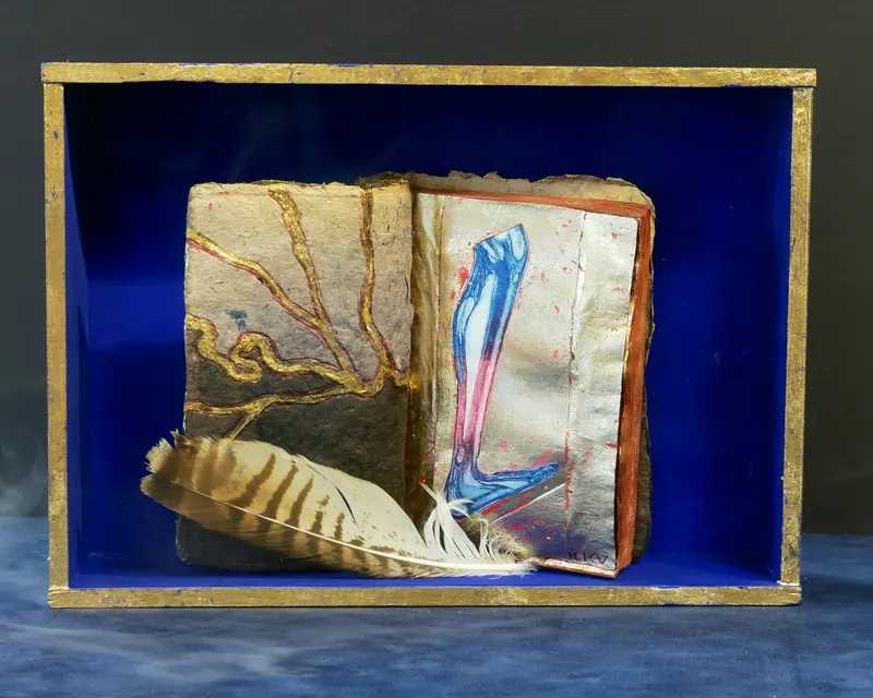 Art de l’objet : un livre peint avec une plume dans une boîte bleue au bord doré